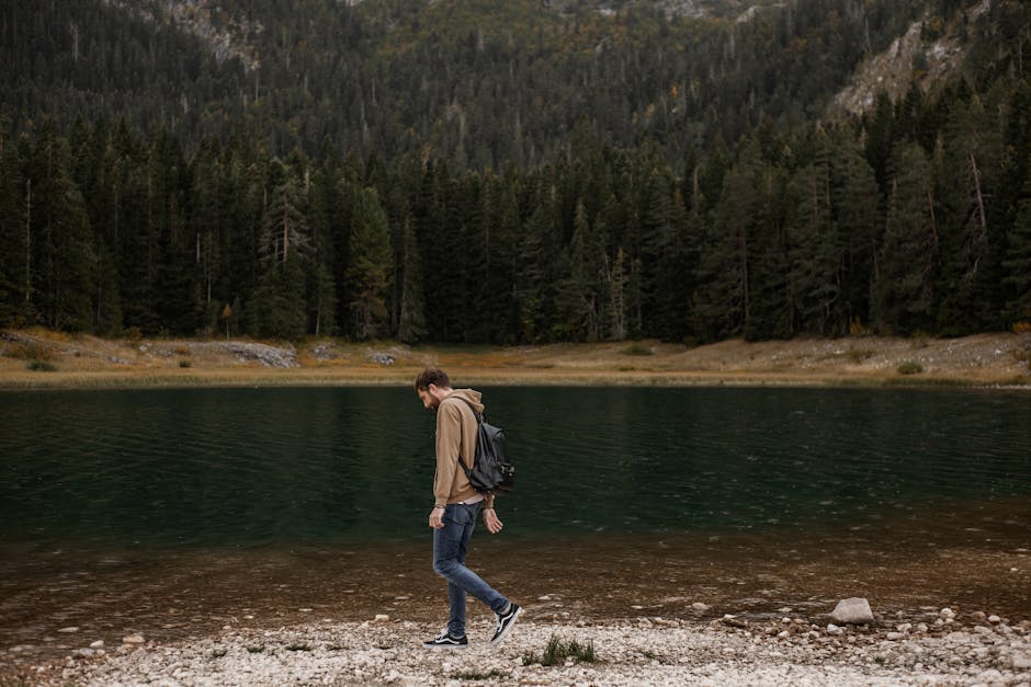 A lone man enjoys a walk by a tranquil mountain lake