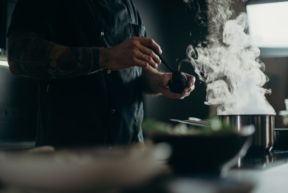 A chef carefully prepares a steamy dish in a professional kitchen setting