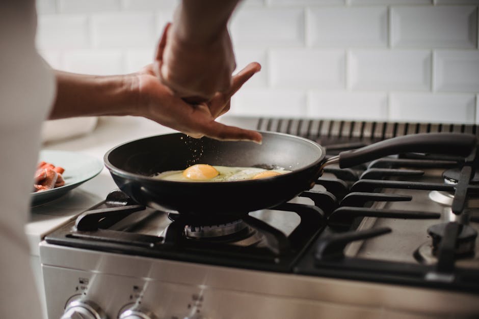 Close-up of frying eggs on a gas stove with hands seasoning the dish