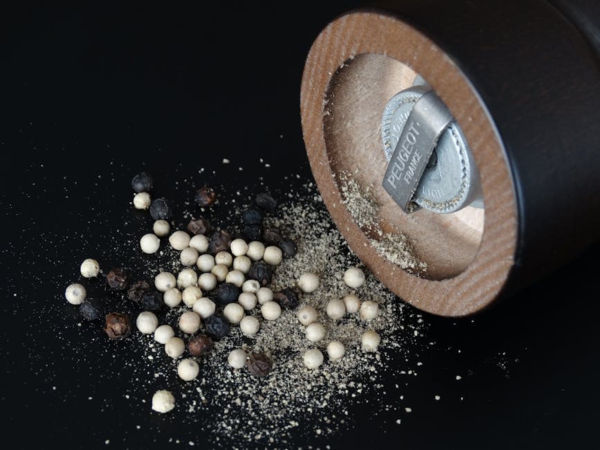 Close-up of a pepper grinder and assorted peppercorns on black surface