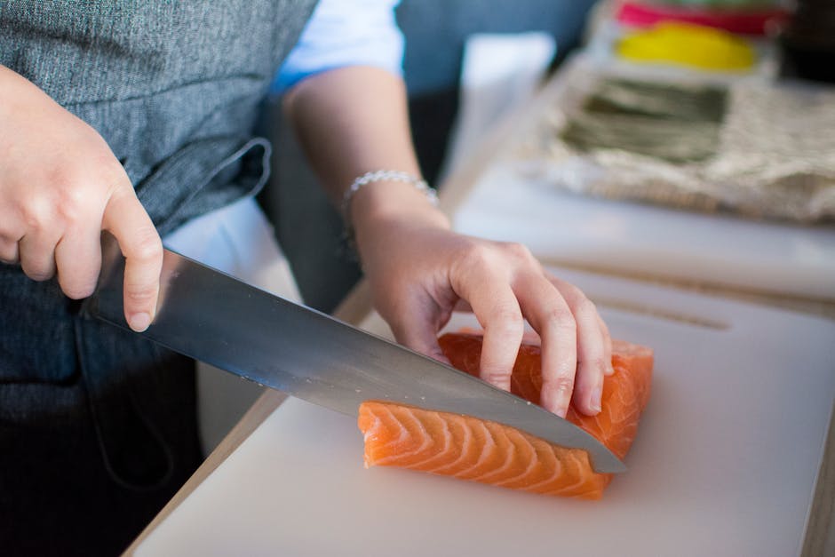 Close-up of a chef's hands slicing fresh salmon for sushi on a cutting board indoors