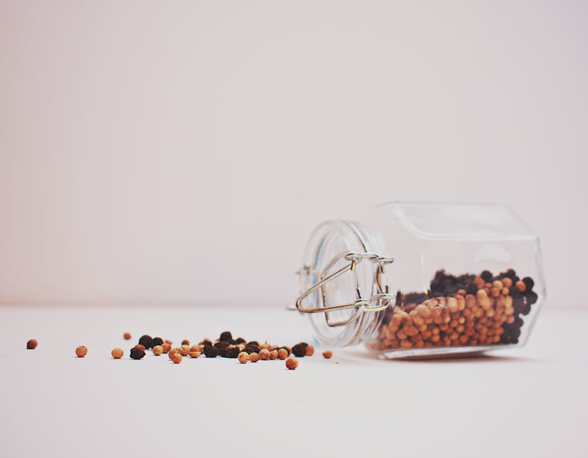 A glass jar tipped over with colorful peppercorns on a minimalist white background