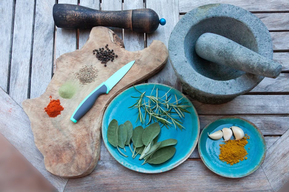 A rustic setup for spice preparation with herbs, spices, garlic, and kitchen tools on wooden table.